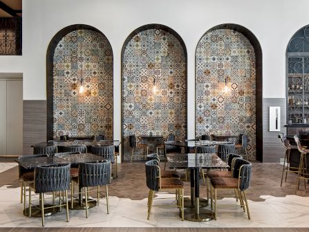 A stylish dining area with patterned tile arches, round tables, and dark upholstered chairs, in a modern, elegant restaurant setting.