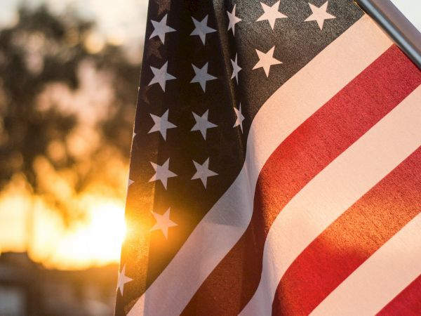 A close-up of an American flag fluttering in the breeze at sunset, stars and stripes glowing warmly as the day ends.