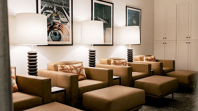 A modern waiting area with tan lounge chairs, matching ottomans, three tall lamps, framed art, and a white cabinet against the wall.